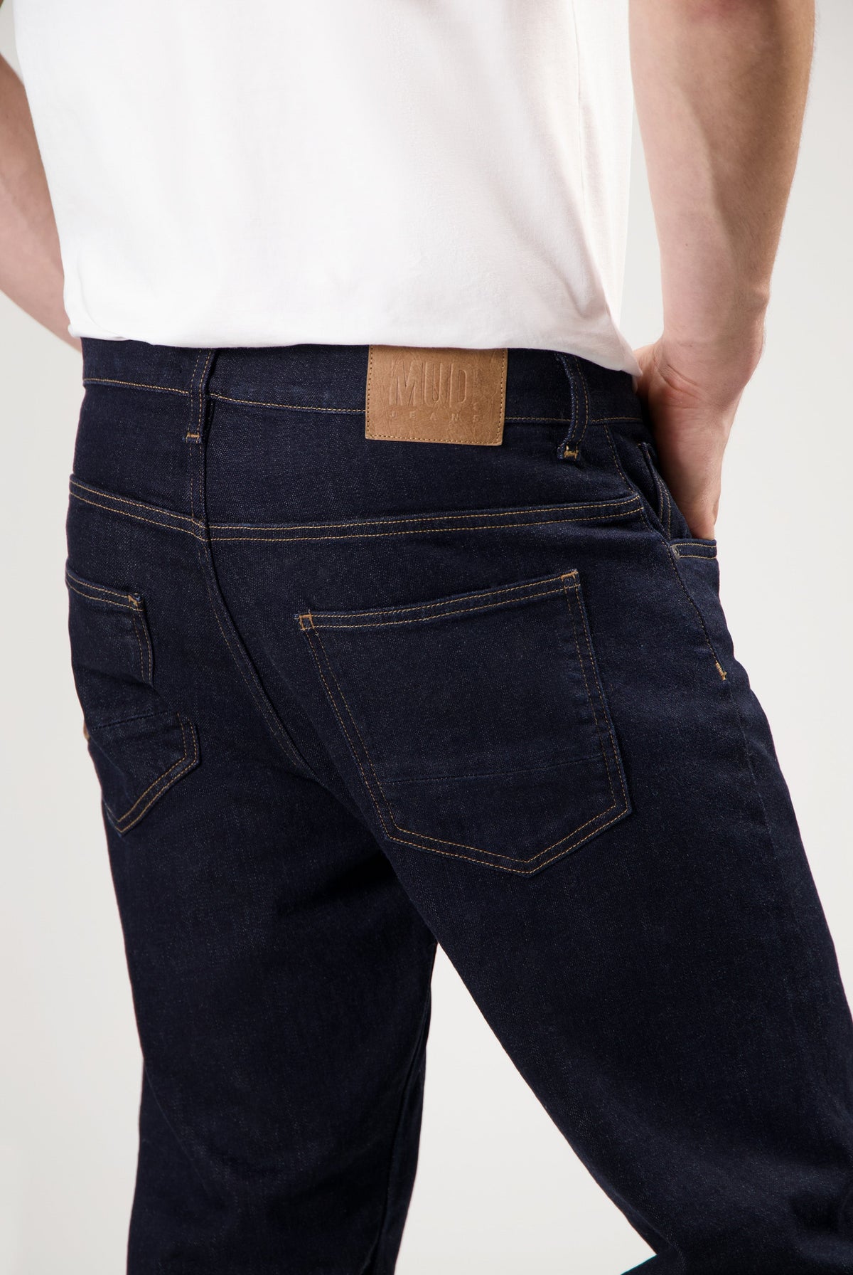 Sustainable MUD Jeans in deep blue denim, crafted from organic cotton, paired with a charcoal gray long-sleeve top.