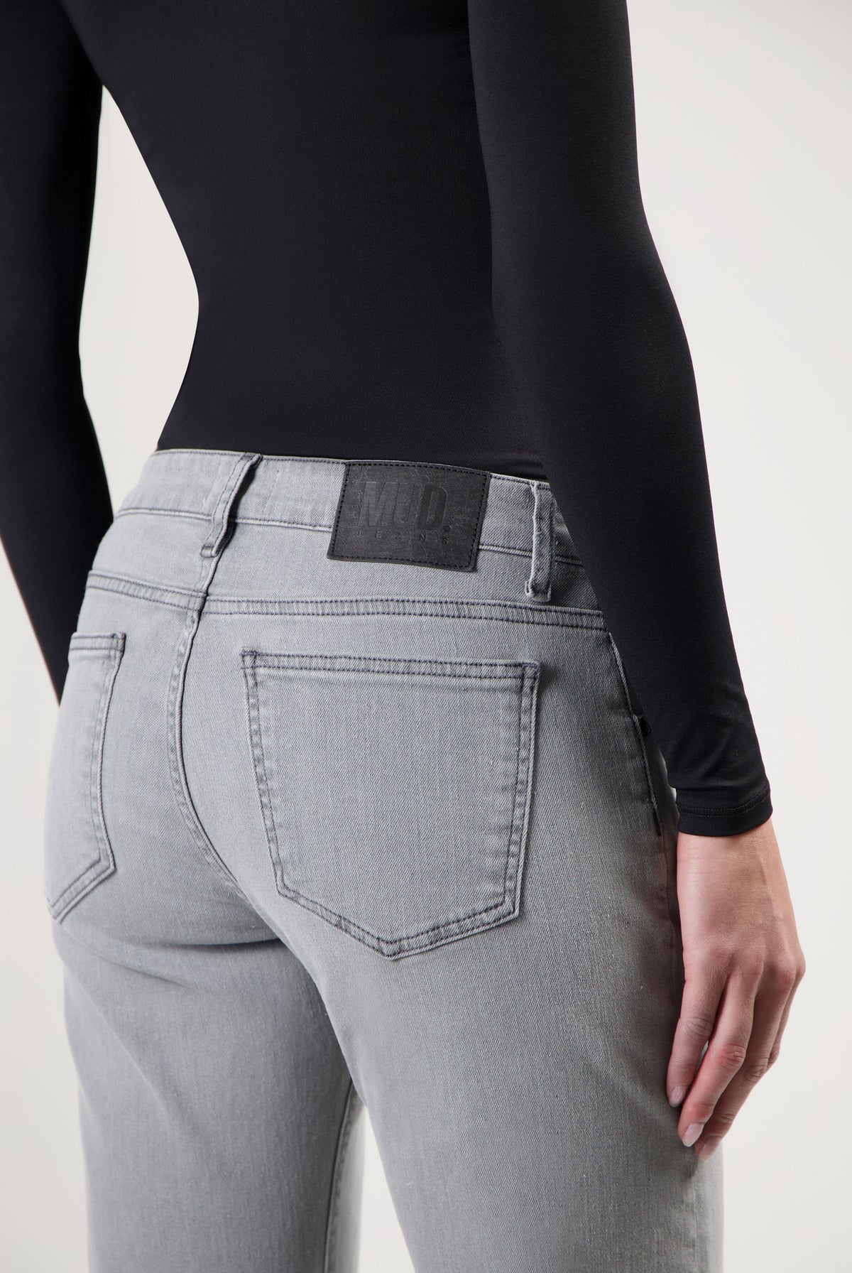 Gray MUD Jeans made from sustainable materials, featuring a rear view of high-waisted denim with a black long-sleeve top.