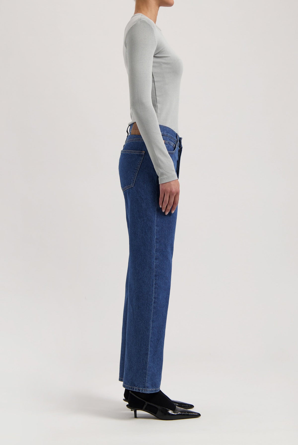 Side view of woman wearing high-waisted blue denim jeans and a light gray long-sleeve top, paired with black heels.