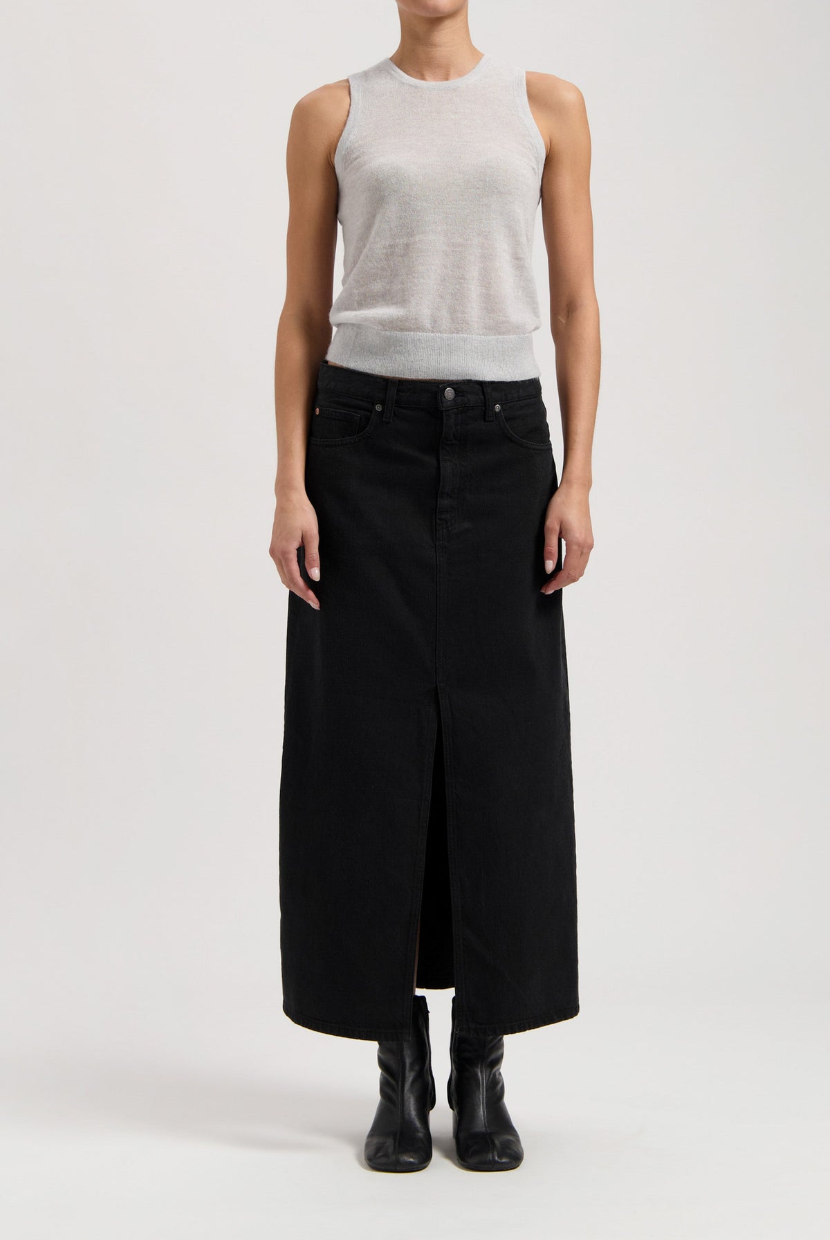 Model wearing a sleeveless gray top with a long black denim skirt, featuring a central slit, and black ankle boots.
