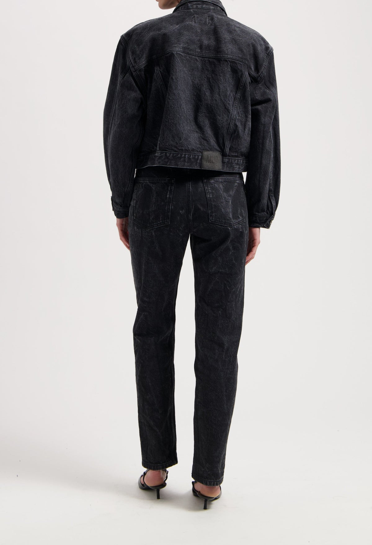 Black denim jacket and jeans set from MUD Jeans, featuring a textured finish, worn with strappy black sandals.