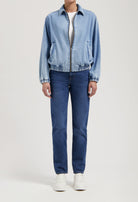 Person wearing a light blue denim jacket with front zipper, paired with dark blue straight-leg jeans and white sneakers.