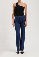One-shoulder black bodysuit styled with classic dark blue high-waisted jeans and black pointed-toe heels.
