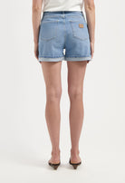 High-waist denim shorts in light blue color with rolled hems, featuring back pockets and worn with a white top and heels.