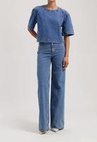 Model wearing blue denim two-piece outfit with short-sleeve top and wide-leg jeans, showcasing casual fashion style.